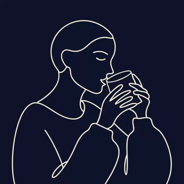 A person cradling the glass in both hands and taking a slow sip.